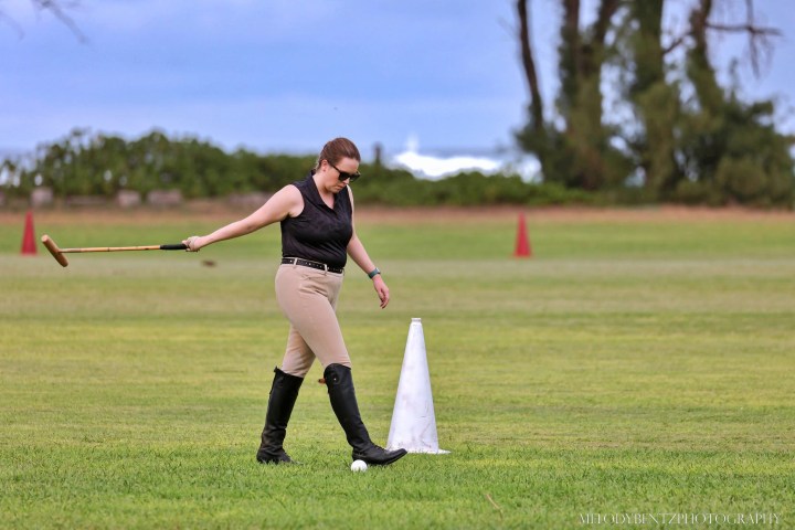 Person practicing polo swings next to a cone on a grassy field.