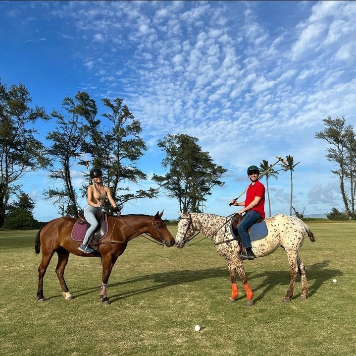 screenshot_20230307_141214_instagram Two people playing polo on horses with mallets, against a scenic background of trees and blue sky.