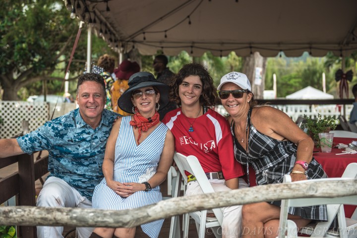 Four people smiling at an outdoor event under a tent.